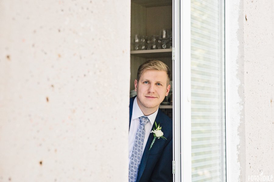 Jaunikis žiūri į vestuvių fotografą pro savo namų langą